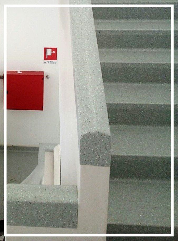 Tromba delle scale con corrimano punteggiato, gradini e una scatola rossa per estintori su una parete bianca.