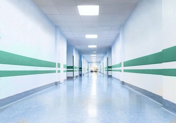 Lungo corridoio vuoto dell'ospedale con una striscia verde, luci fluorescenti e pavimento lucido.