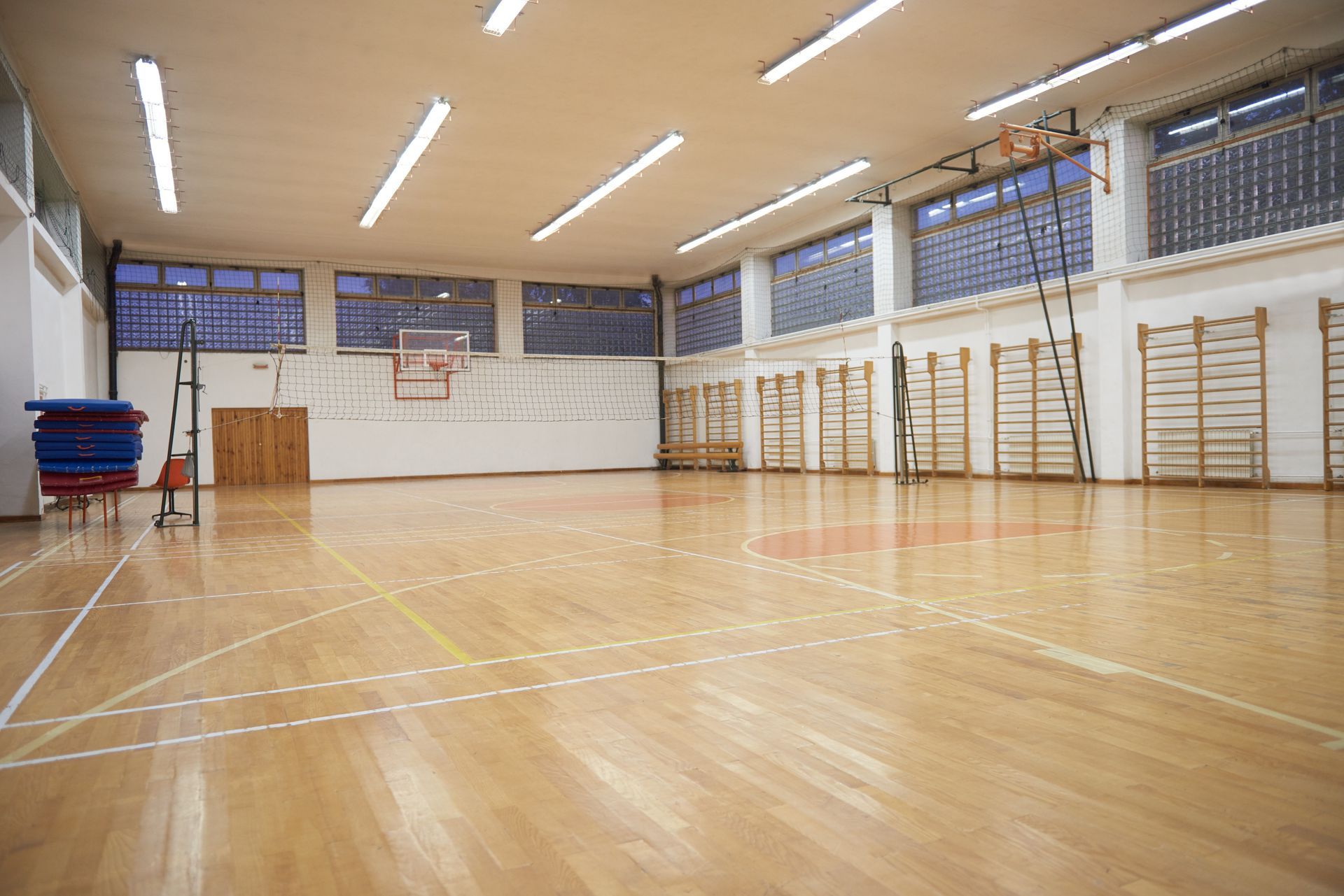 Palestra vuota con pavimento in legno, canestro da basket, spalliera svedese e luci dall'alto.
