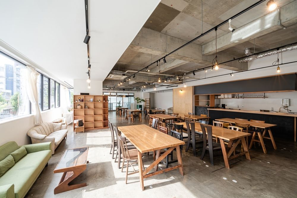 Interior view of a modern co-working space with tables, a sofa, and a kitchen area.