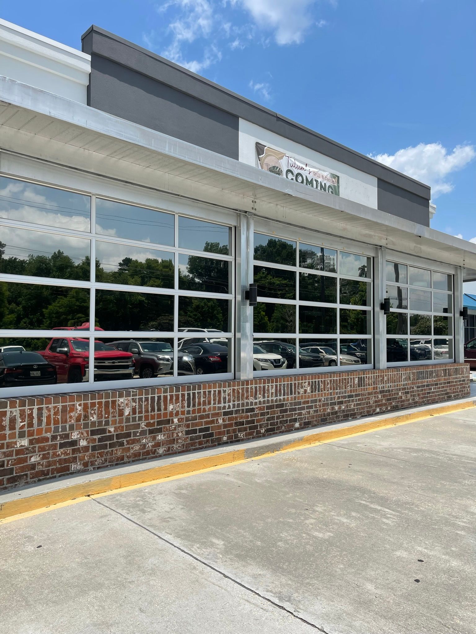Building with glass garage doors, brick facade, and parked cars, likely a business.