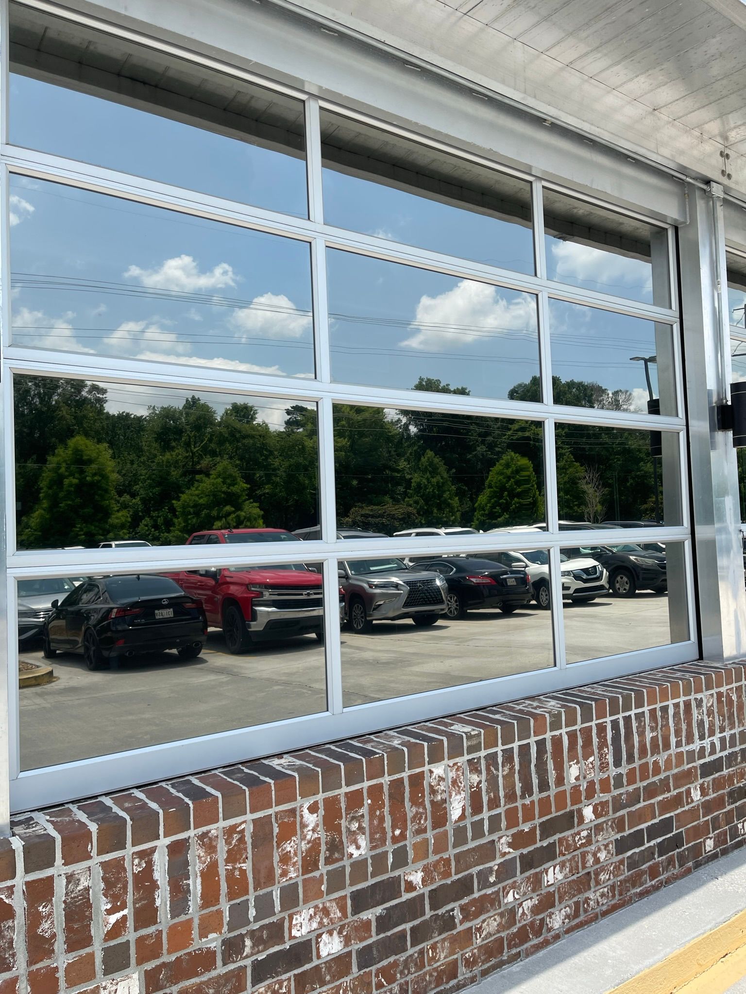 Glass window reflecting trees, sky, and parked cars against a brick building.