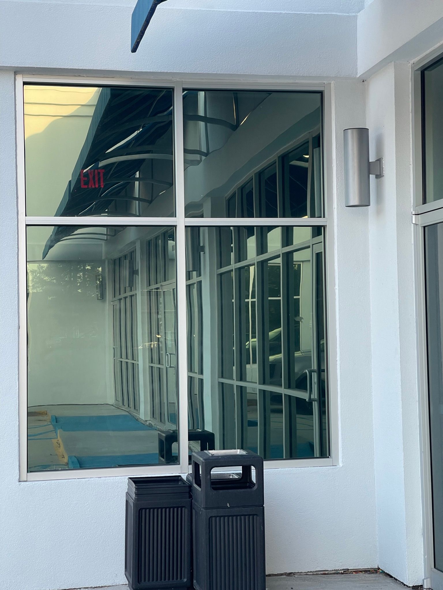 Exterior view of building with tinted windows, an exit sign visible. Trash cans sit below.