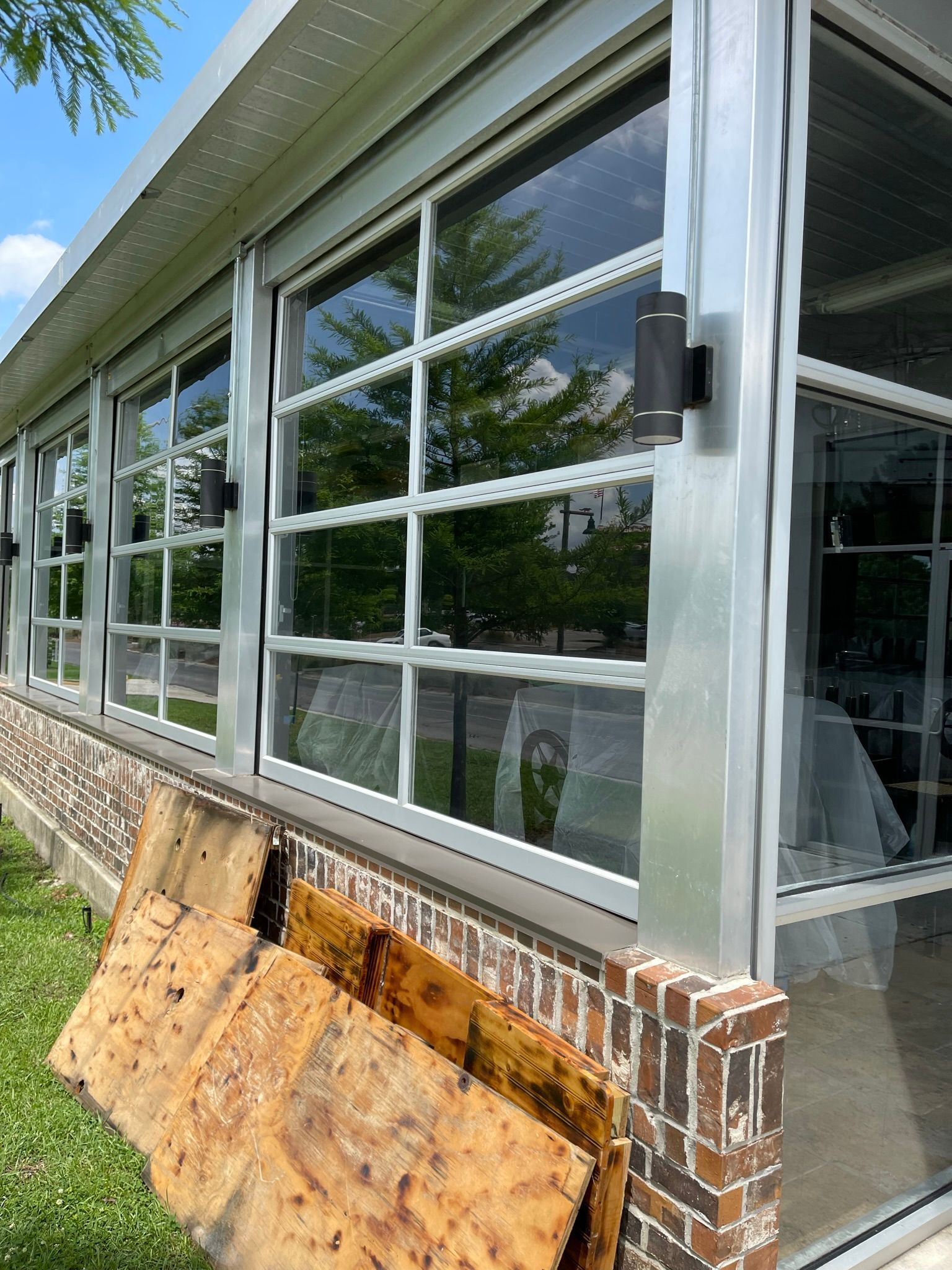Long row of windows with white grid patterns, on a brick and aluminum building.  Sheets of wood on the ground.