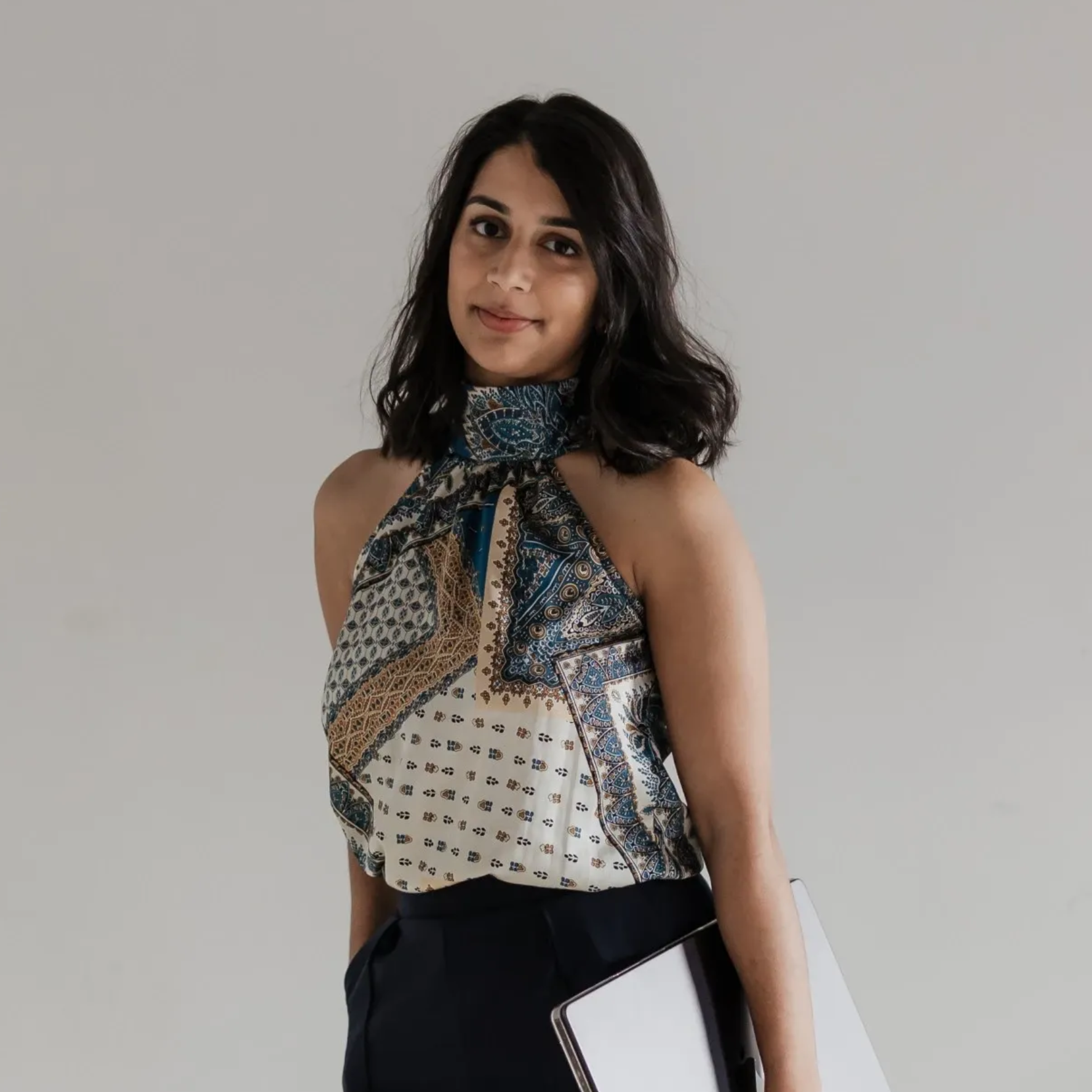 Woman posing against a white background, wearing a patterned halter top and black pants