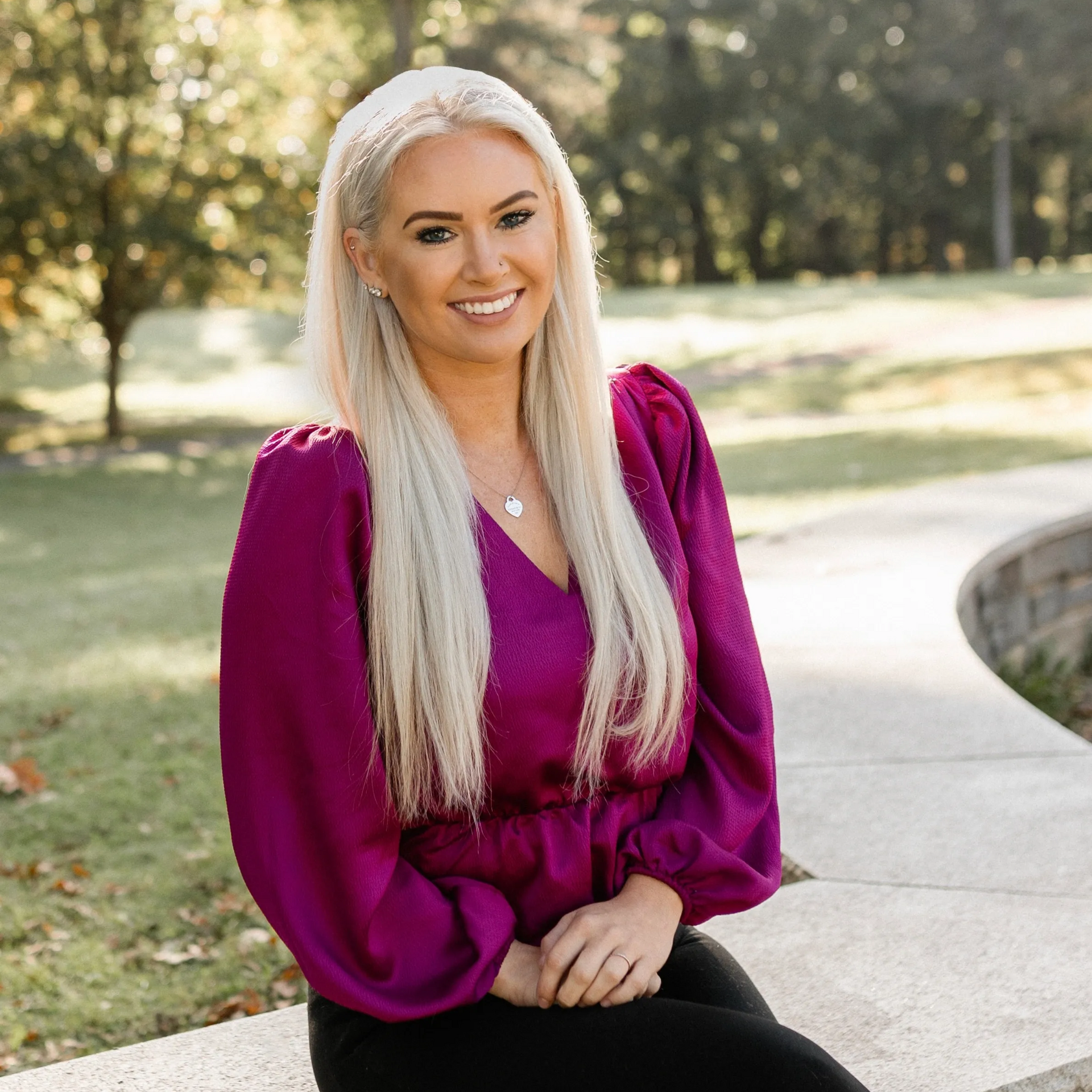 Woman in pink cardigan sitting on park bench, smiling.