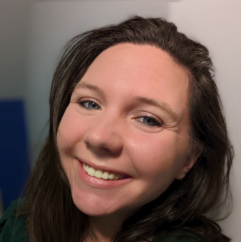 A woman in a green sweater is smiling for the camera.