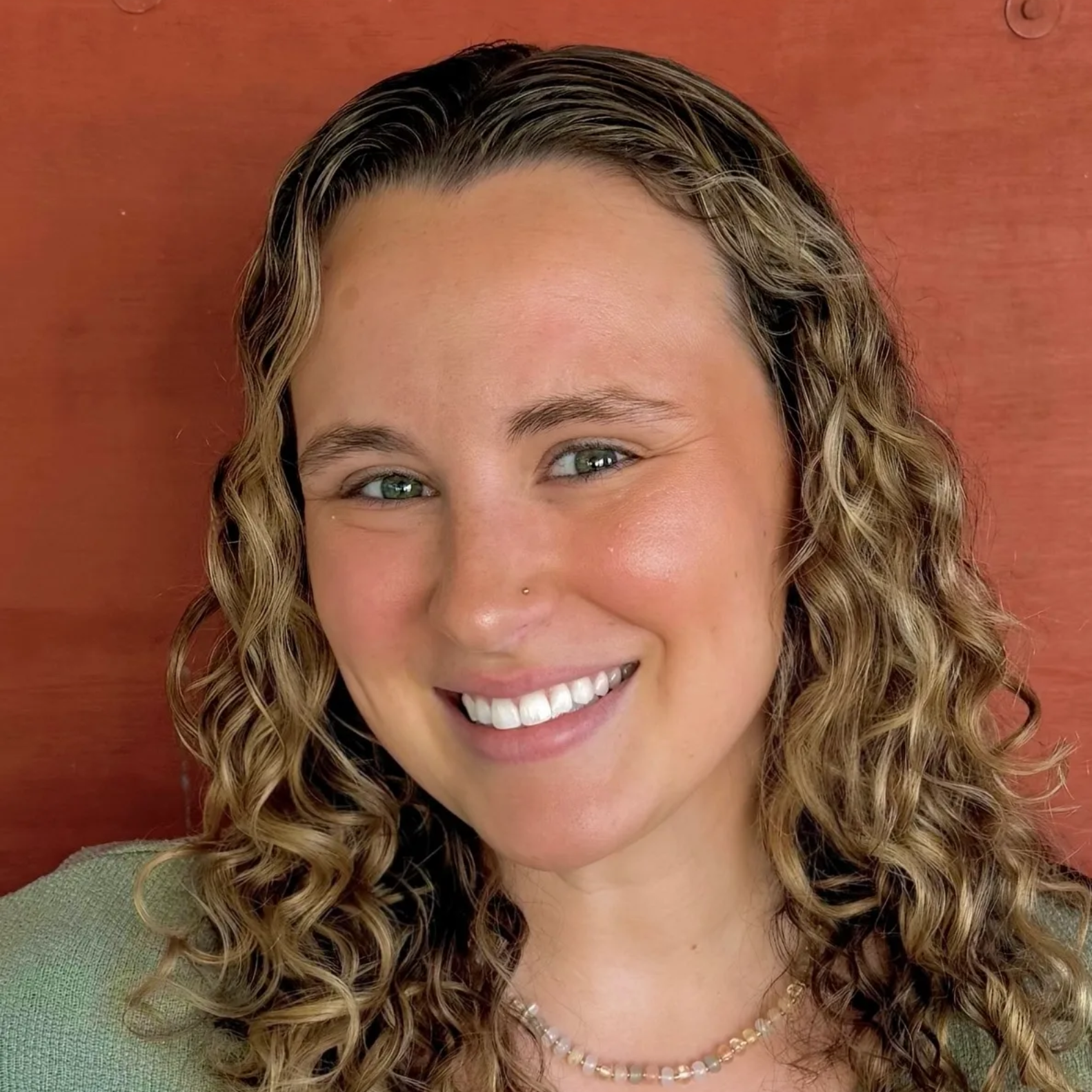 Smiling person with curly hair against a terracotta background.