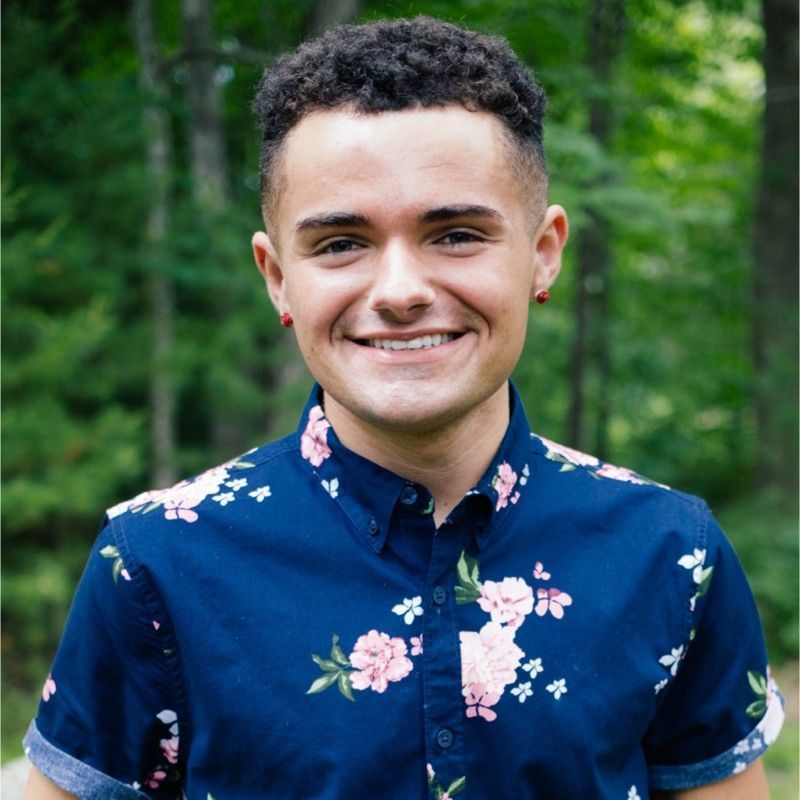 A young man wearing a blue floral shirt is smiling for the camera.
