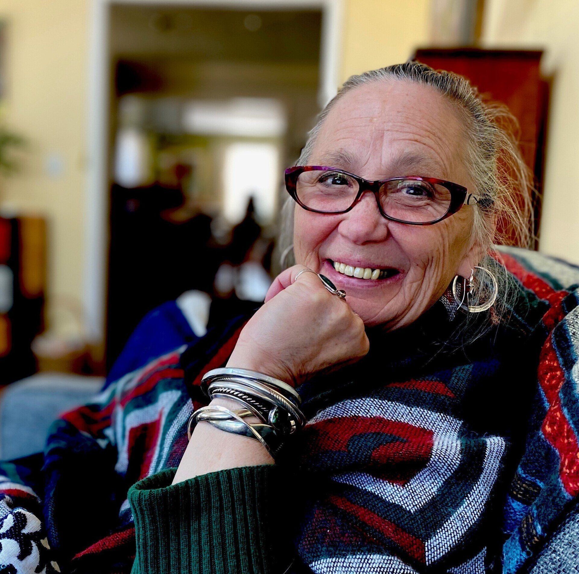 An older woman wearing glasses and bracelets smiles for the camera