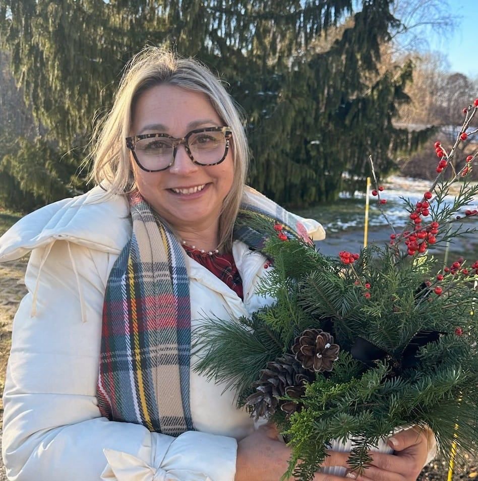 A woman wearing glasses and a plaid scarf is holding a bouquet of christmas decorations.