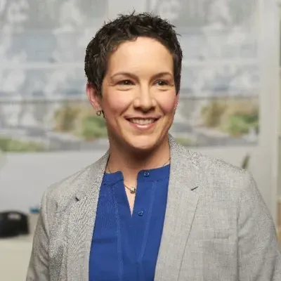 Smiling person in a gray blazer and blue shirt in an office setting