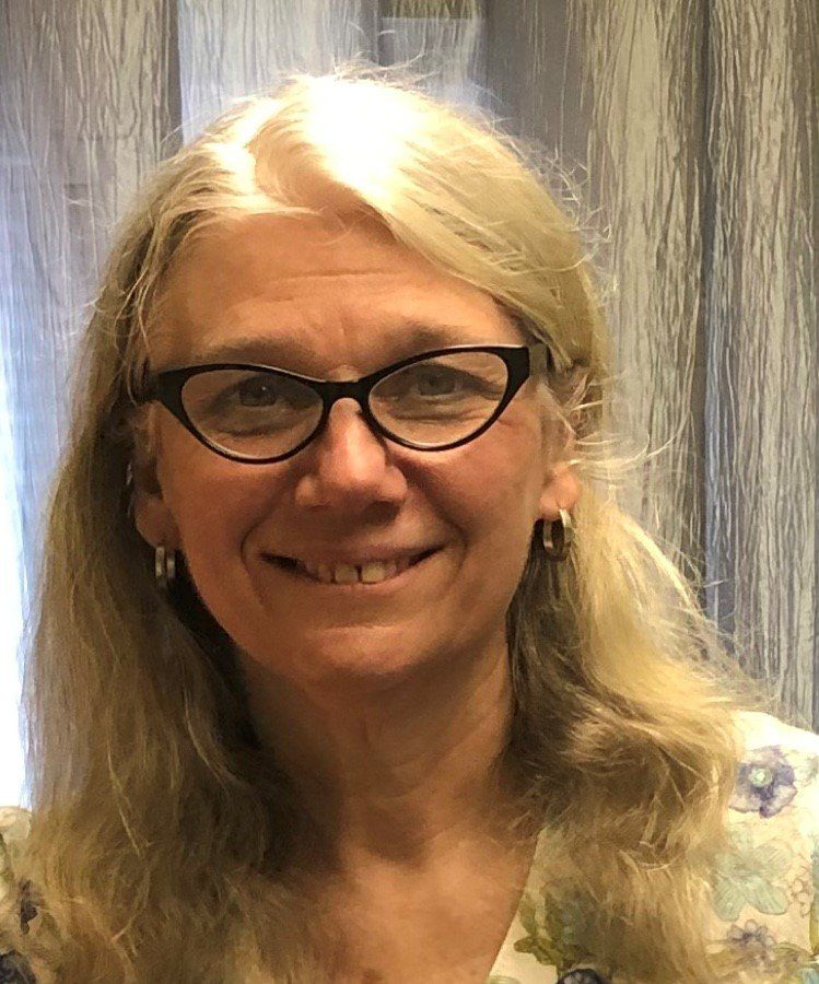 A woman wearing glasses and earrings is smiling for the camera.