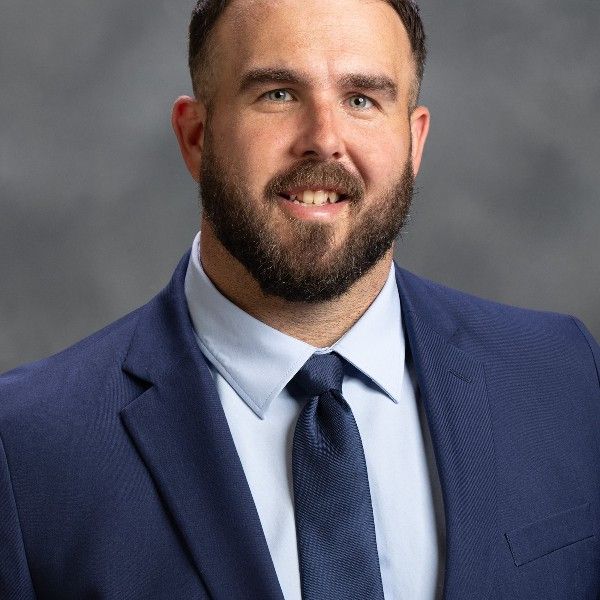 A man with a beard is wearing a blue suit and tie.