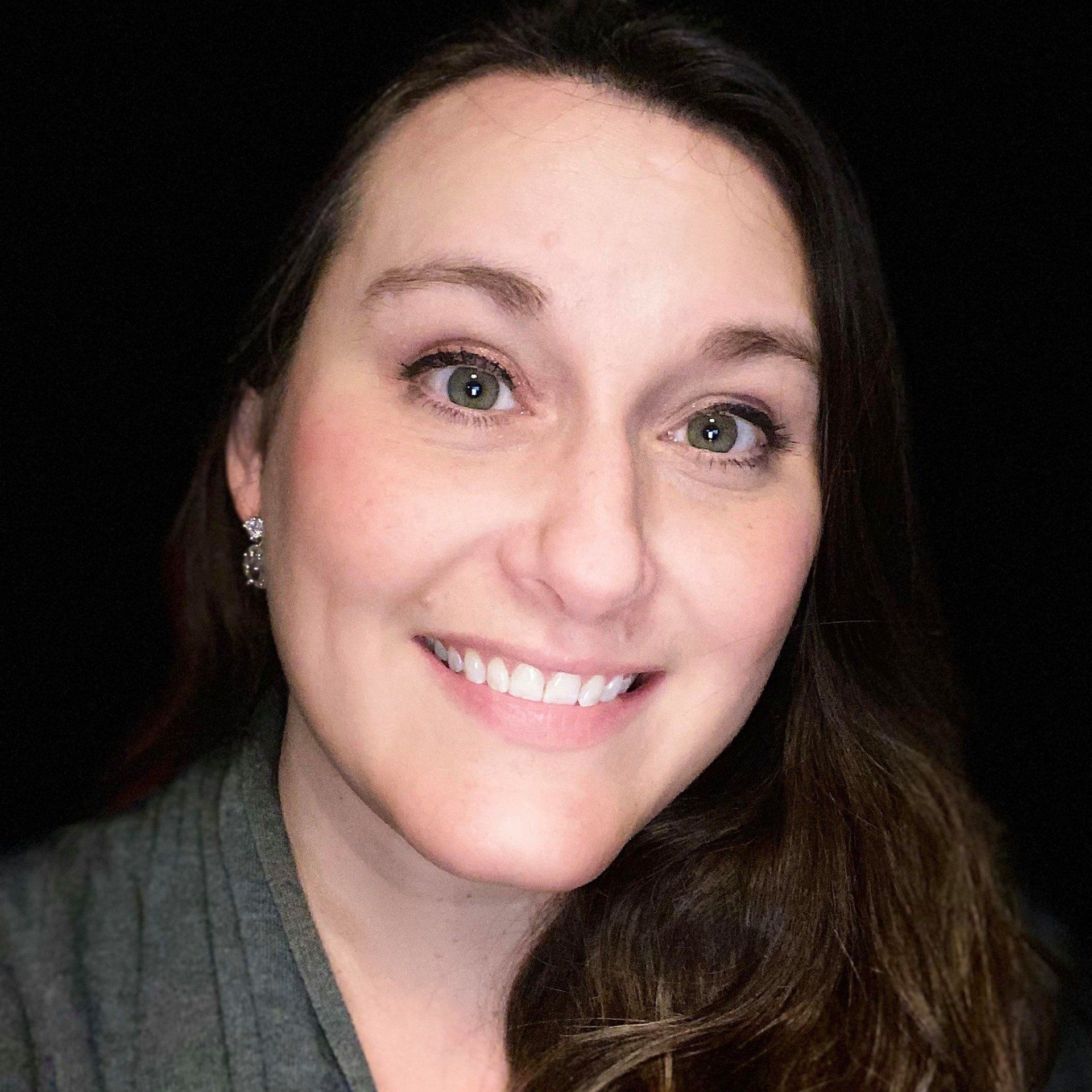 A woman is smiling for the camera in front of a black background.