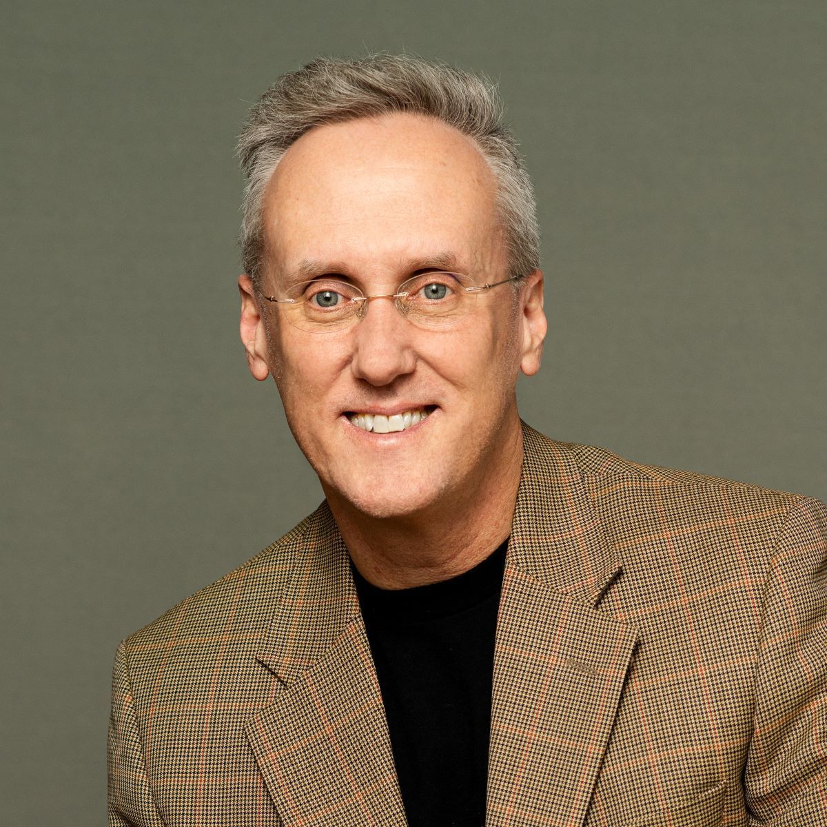 A man wearing glasses and a plaid jacket smiles for the camera