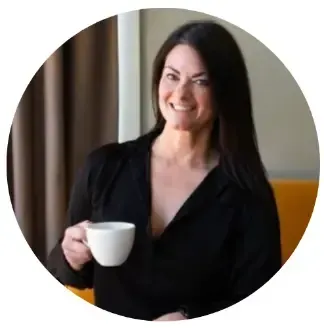 Smiling person in a black top holding a white mug by a window