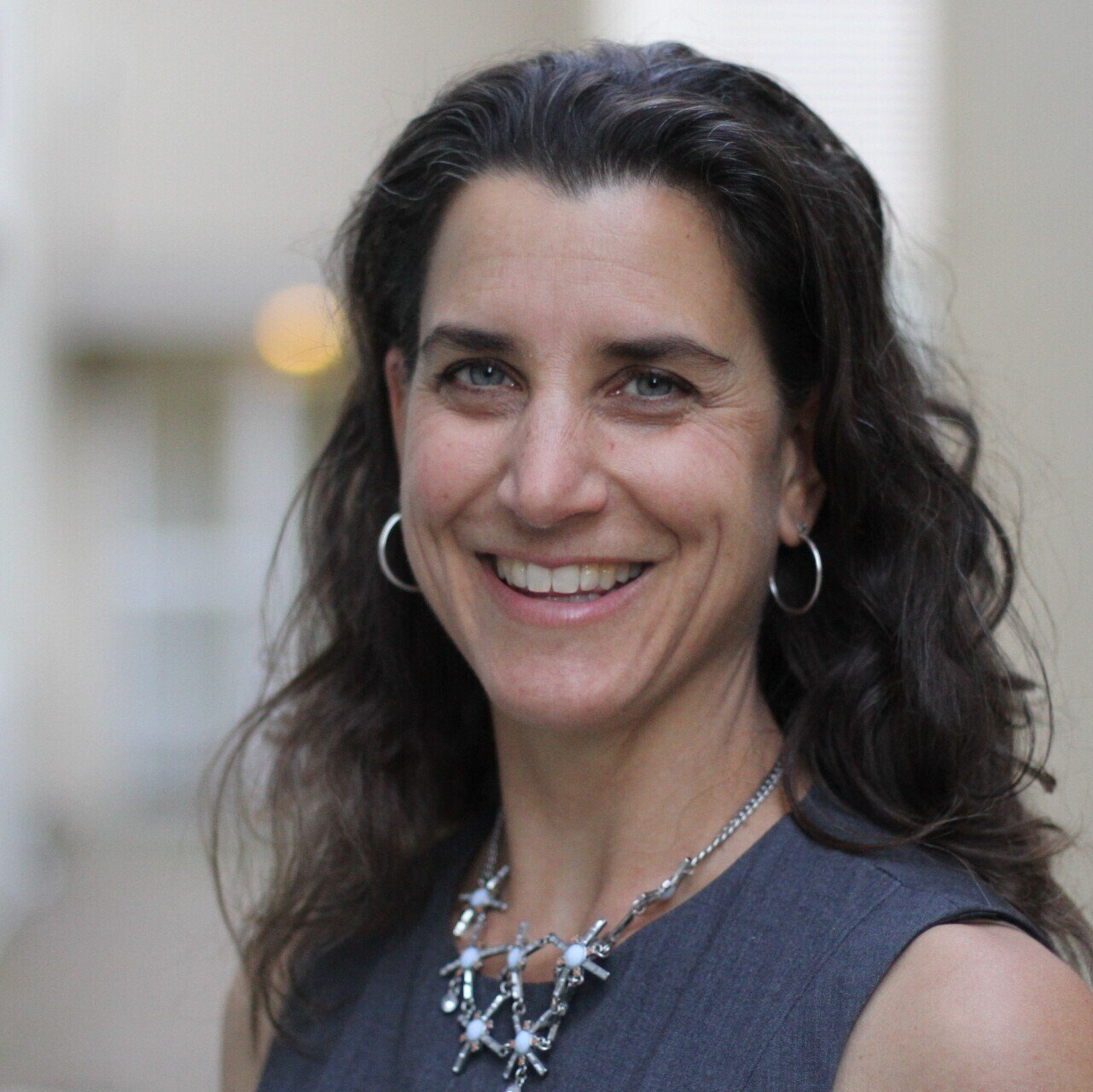 A woman wearing a necklace and hoop earrings smiles for the camera