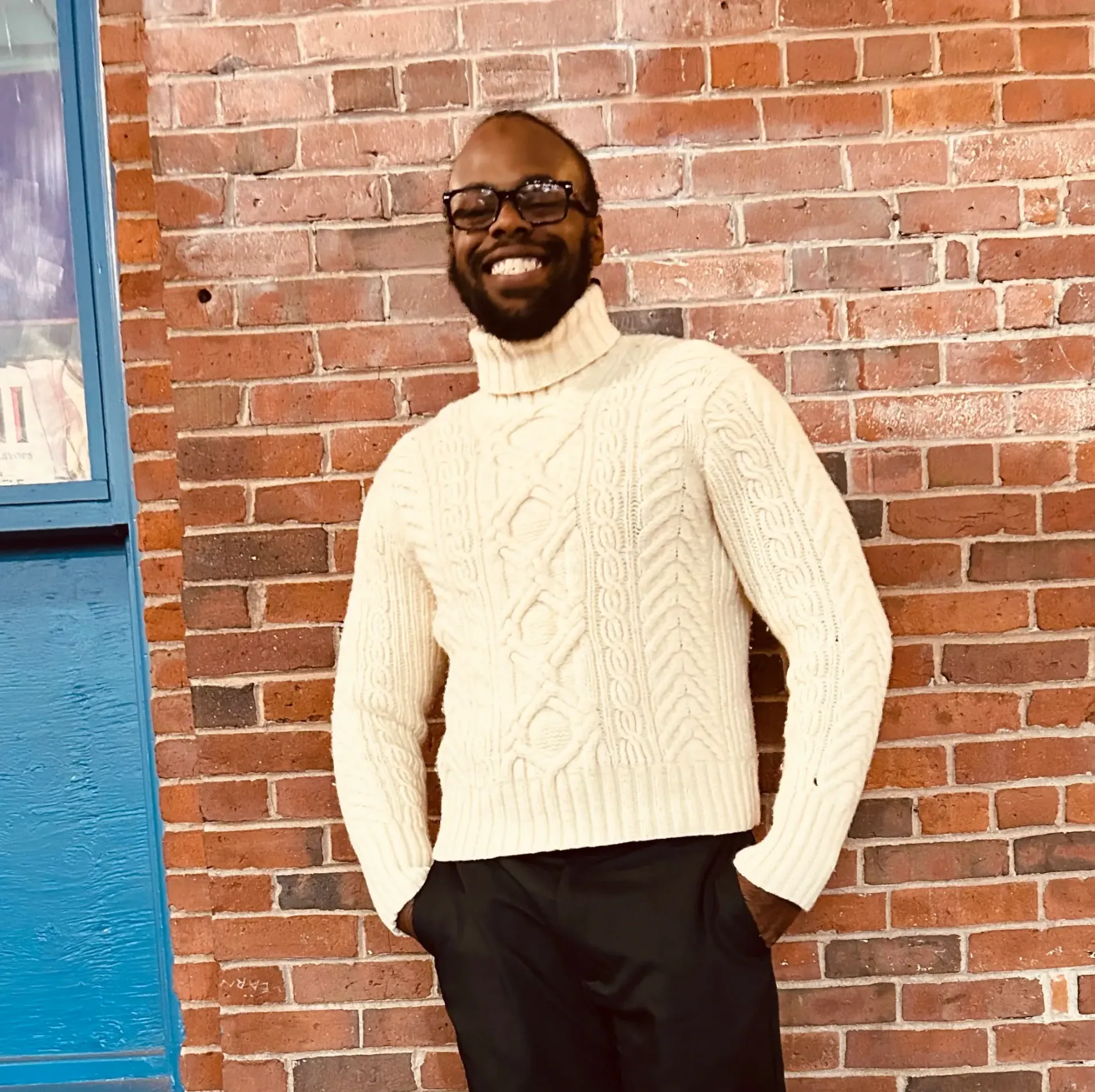 A man in a suit and tie is smiling in front of a brick wall.