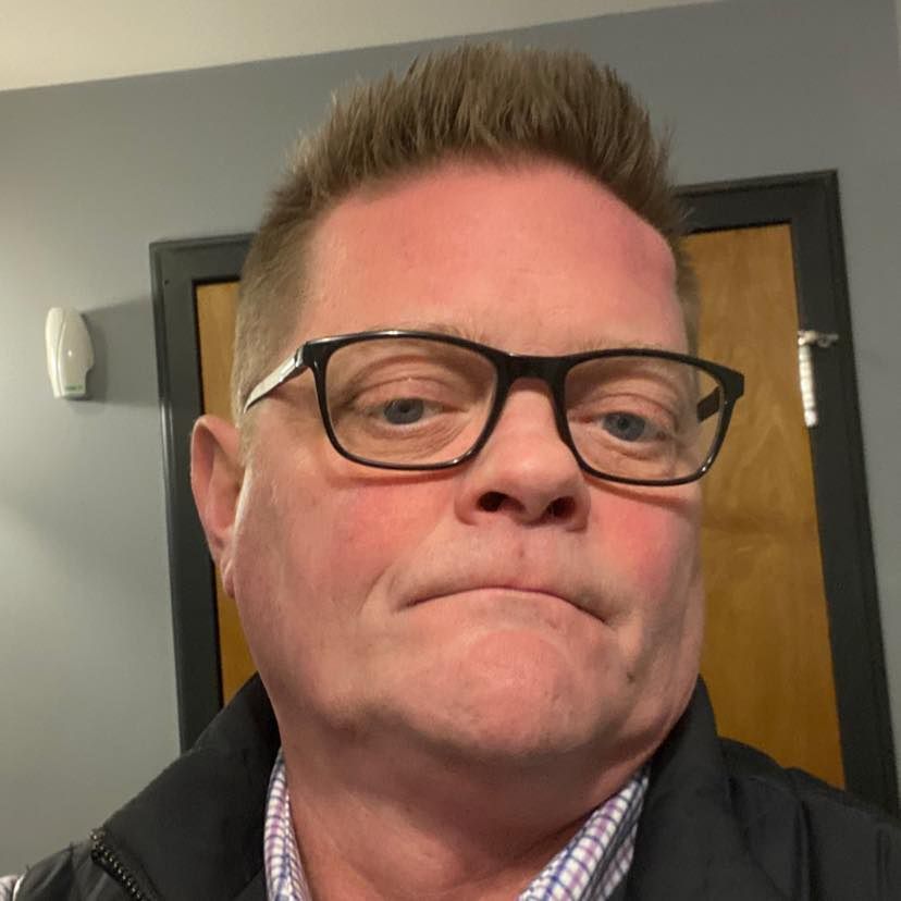 A man wearing glasses and a jacket is making a funny face.