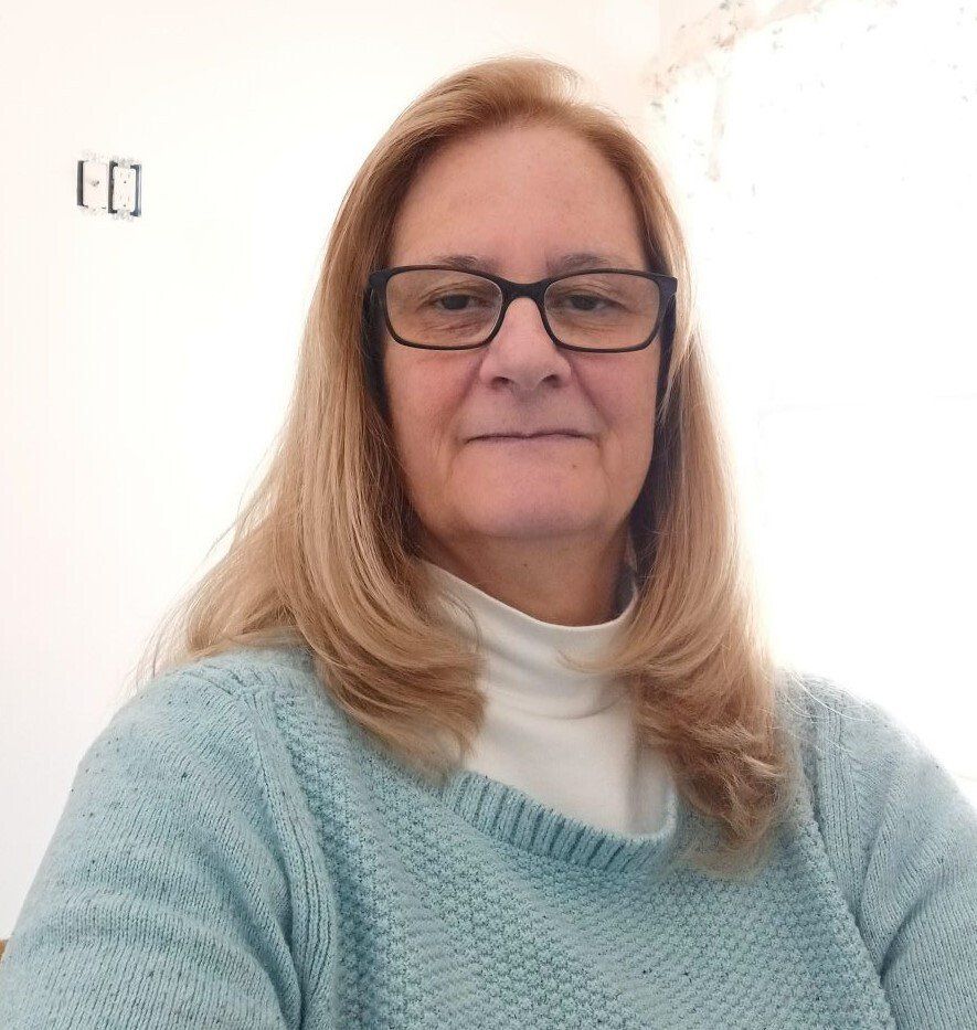 A woman wearing glasses and a blue sweater is looking at the camera.
