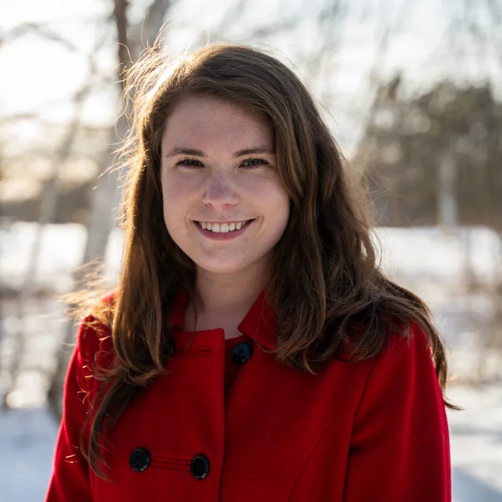 Woman in red coat smiles outside in snowy setting.
