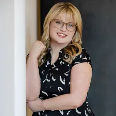 A woman wearing glasses and a red sweater is smiling for the camera.