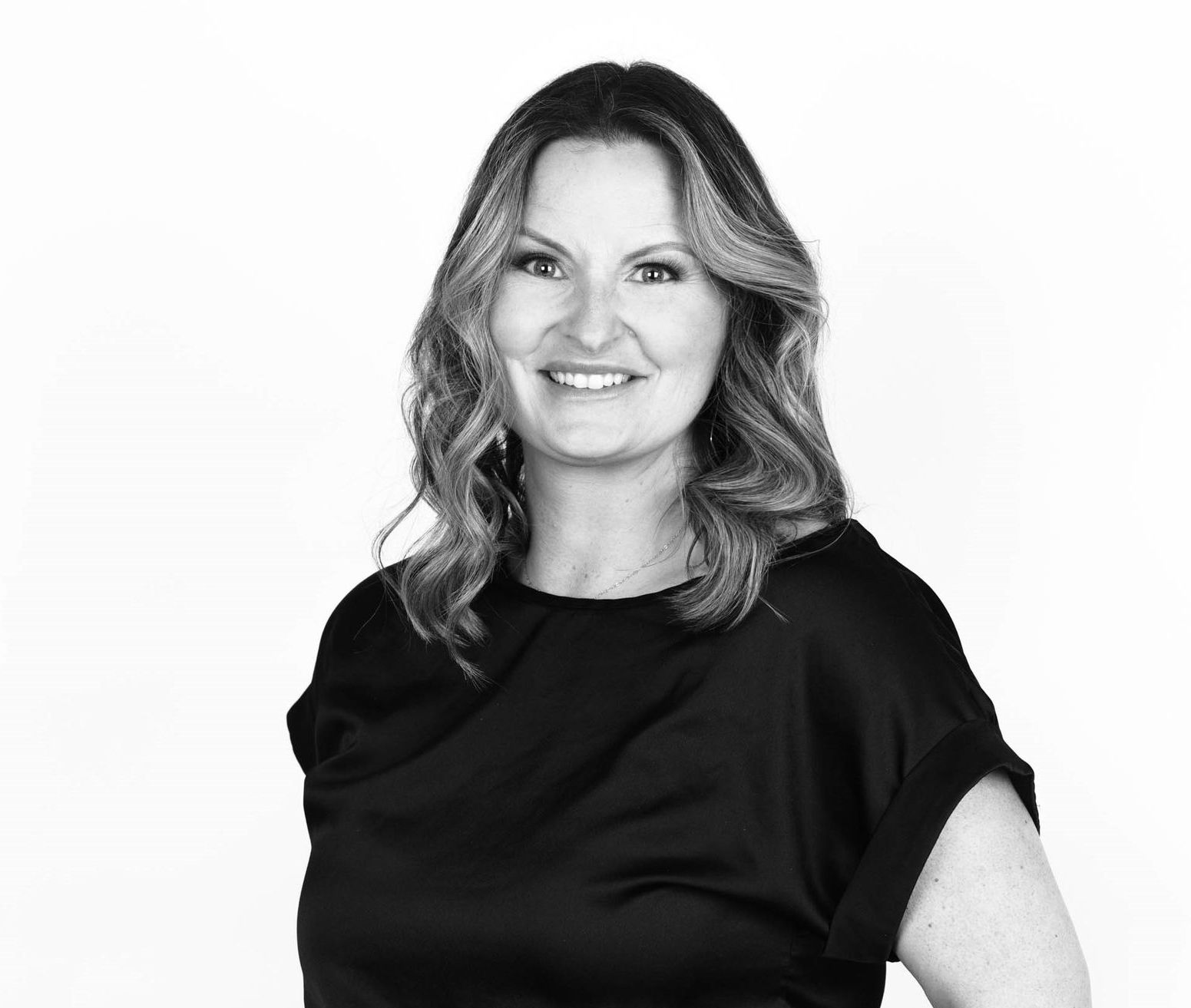 A woman in a black shirt is smiling in a black and white photo.