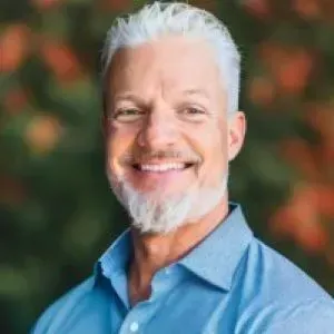 Smiling man in a blue shirt against a blurred green and orange background