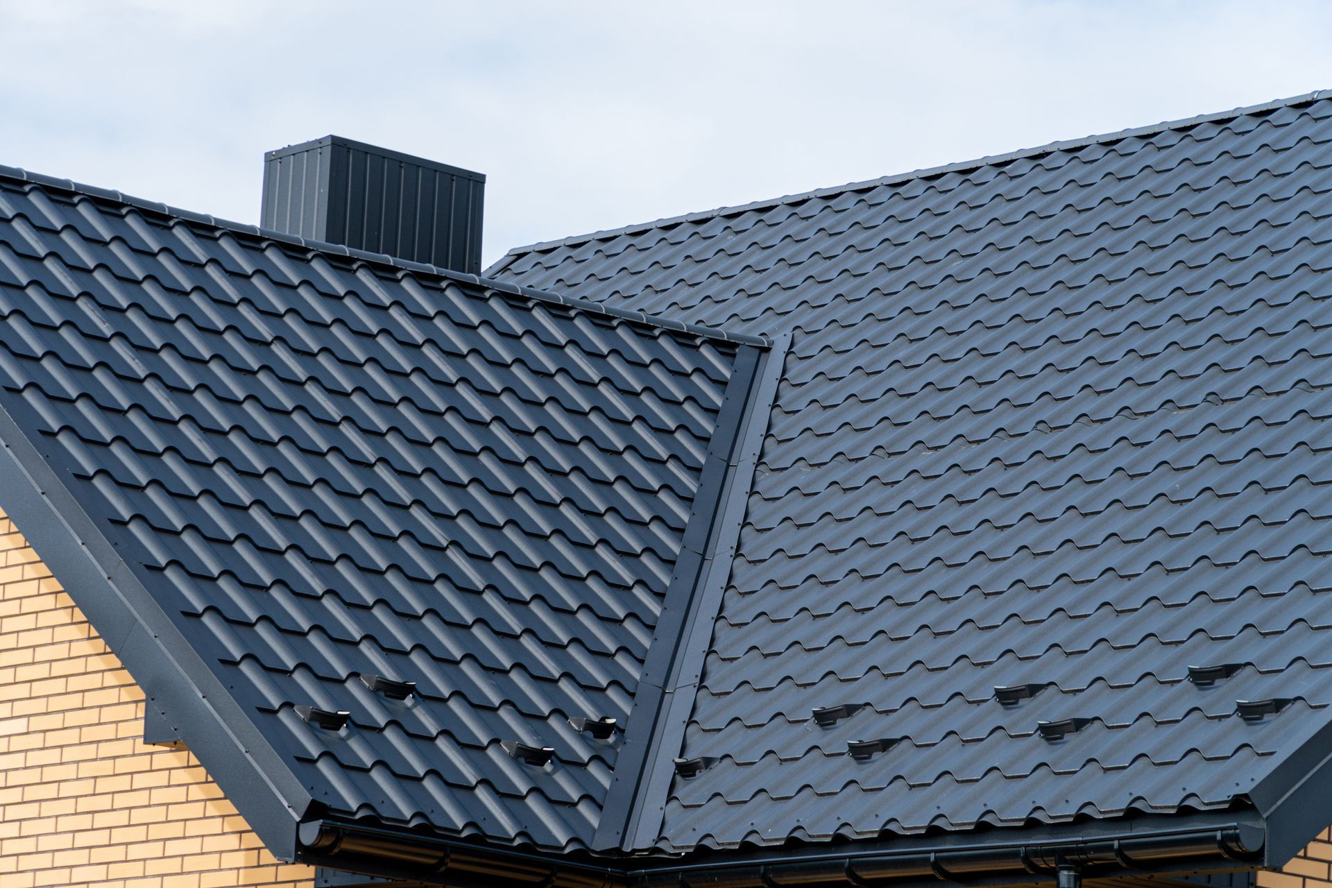 Dark gray tiled roof with a rooftop vent on a brick house