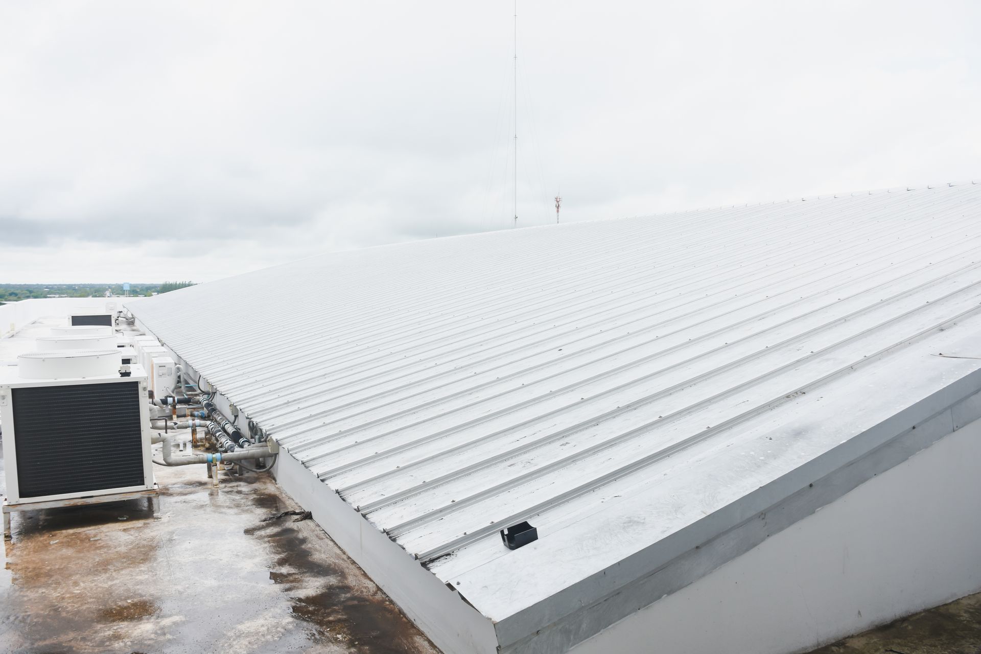 Snow-covered industrial rooftop with white metal panels and a wet walkway under an overcast sky