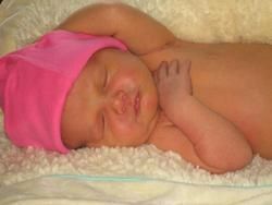 Newborn wearing a pink hat, sleeping on a fluffy white blanket.