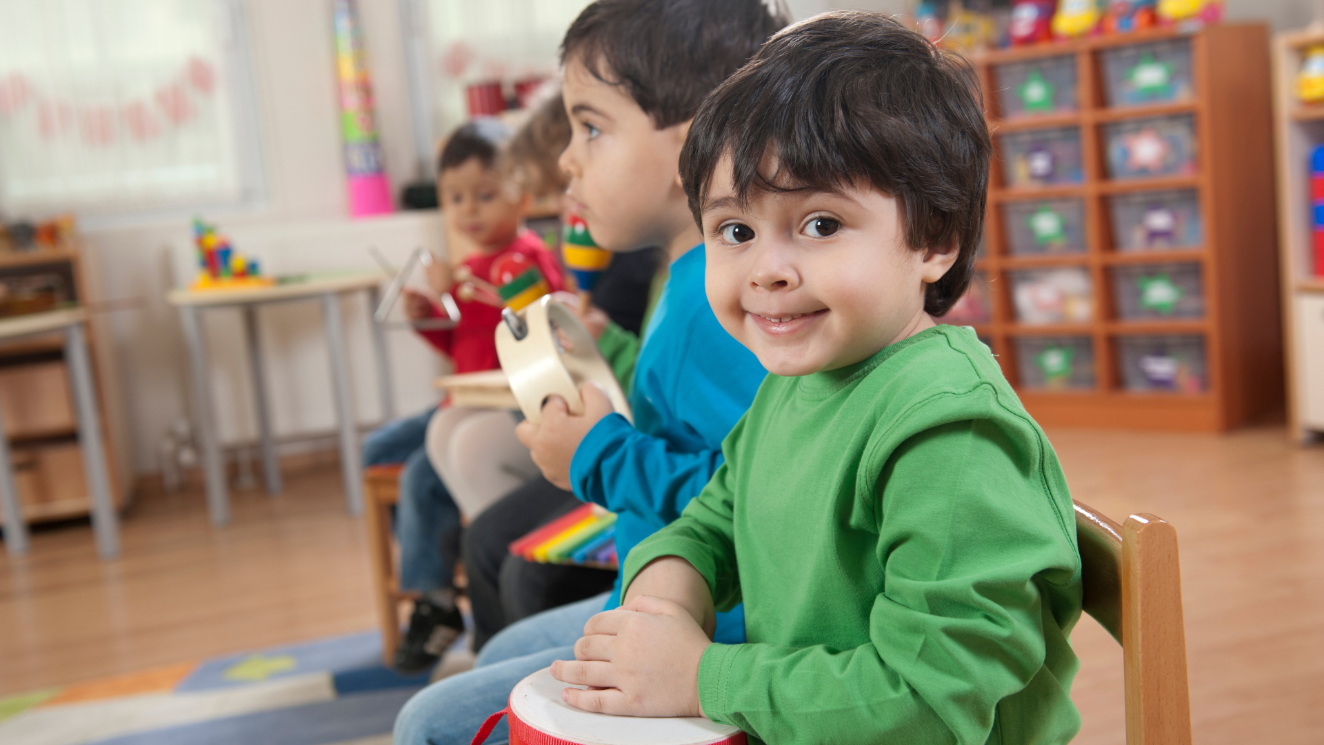Children in a music class, playing instruments. One boy smiles, holding a drum.