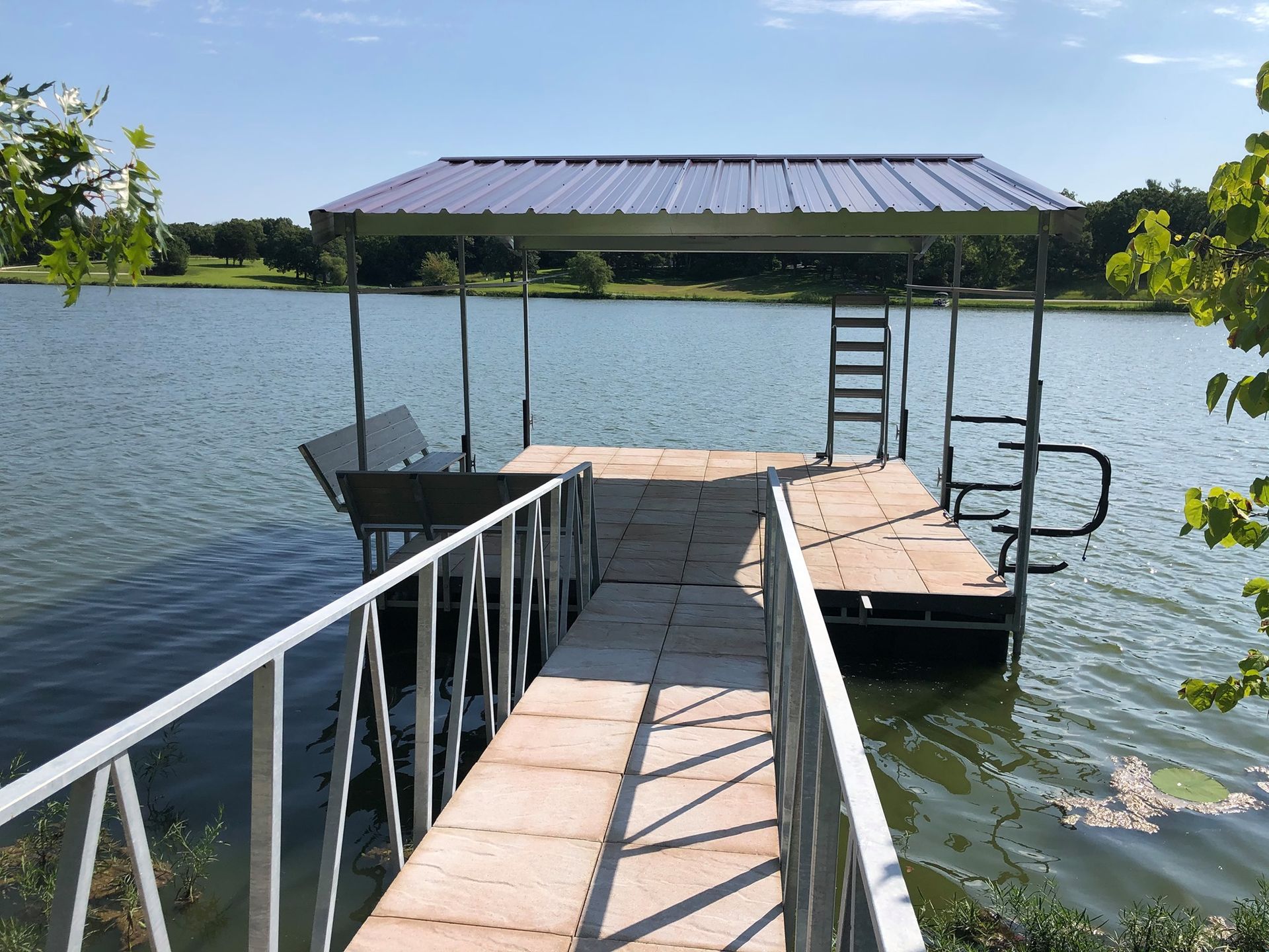 Floating dock with a metal-roof shelter extending into a calm lake on a sunny day