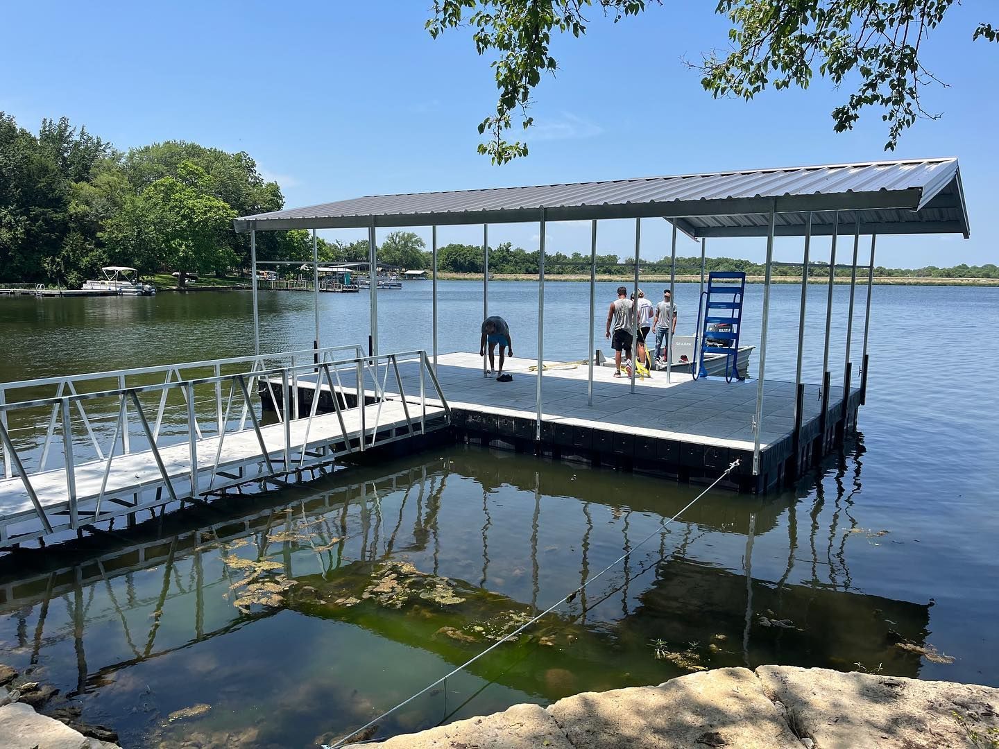 People on a floating dock with a canopy beside a calm lake on a sunny day