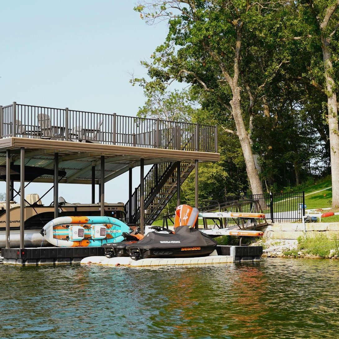 Waterfront dock with a jet ski and colorful inflatable raft beside a wooden boathouse and trees
