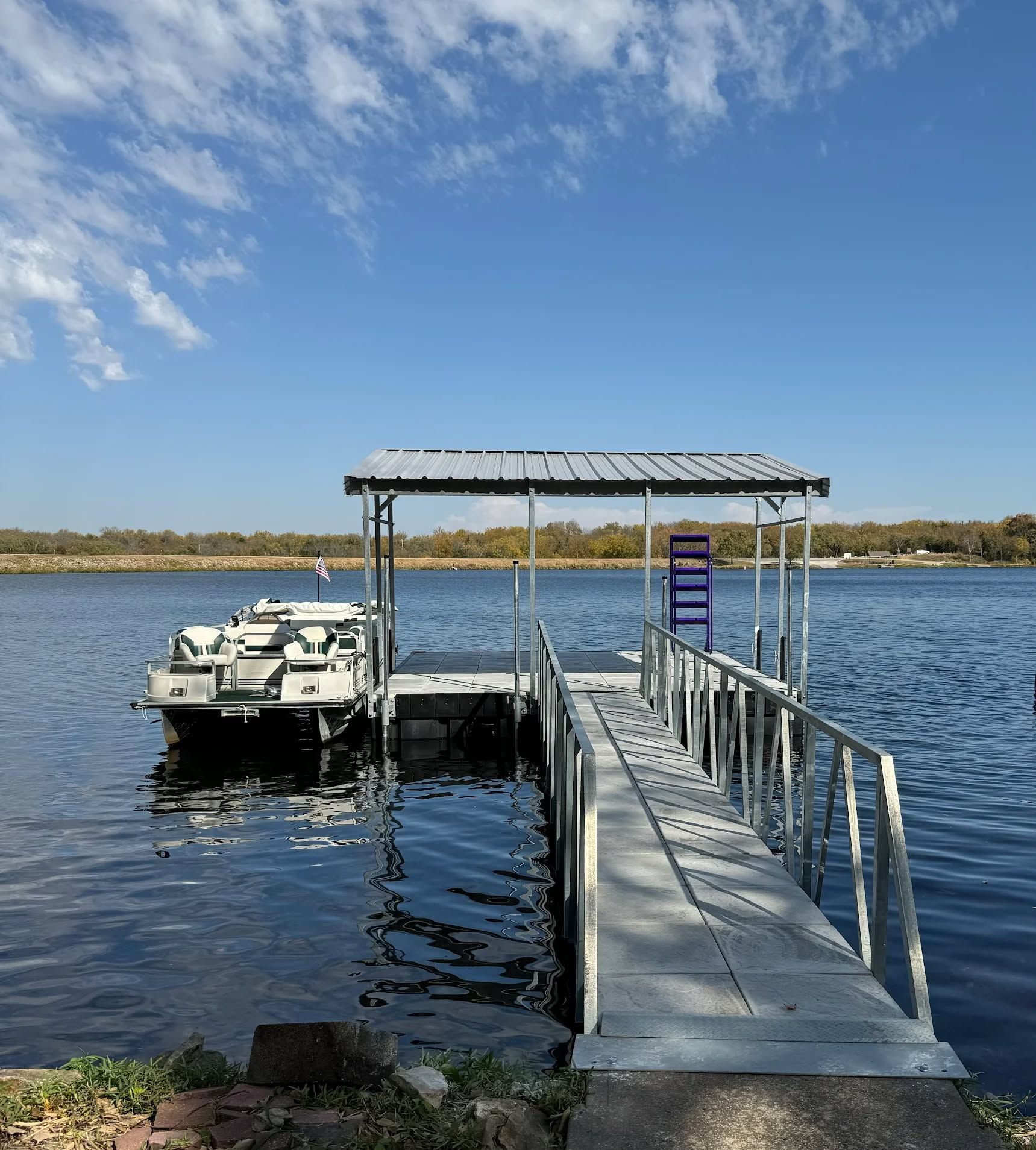 Covered dock with a small boat on calm water under a blue sky
