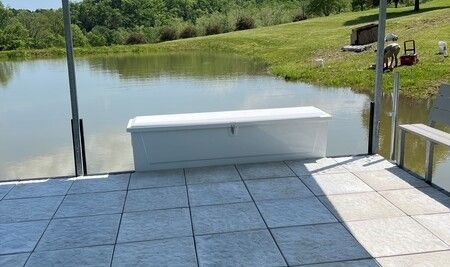 Patio overlooking a calm pond, with blue-tiled flooring and a white bench in the foreground
