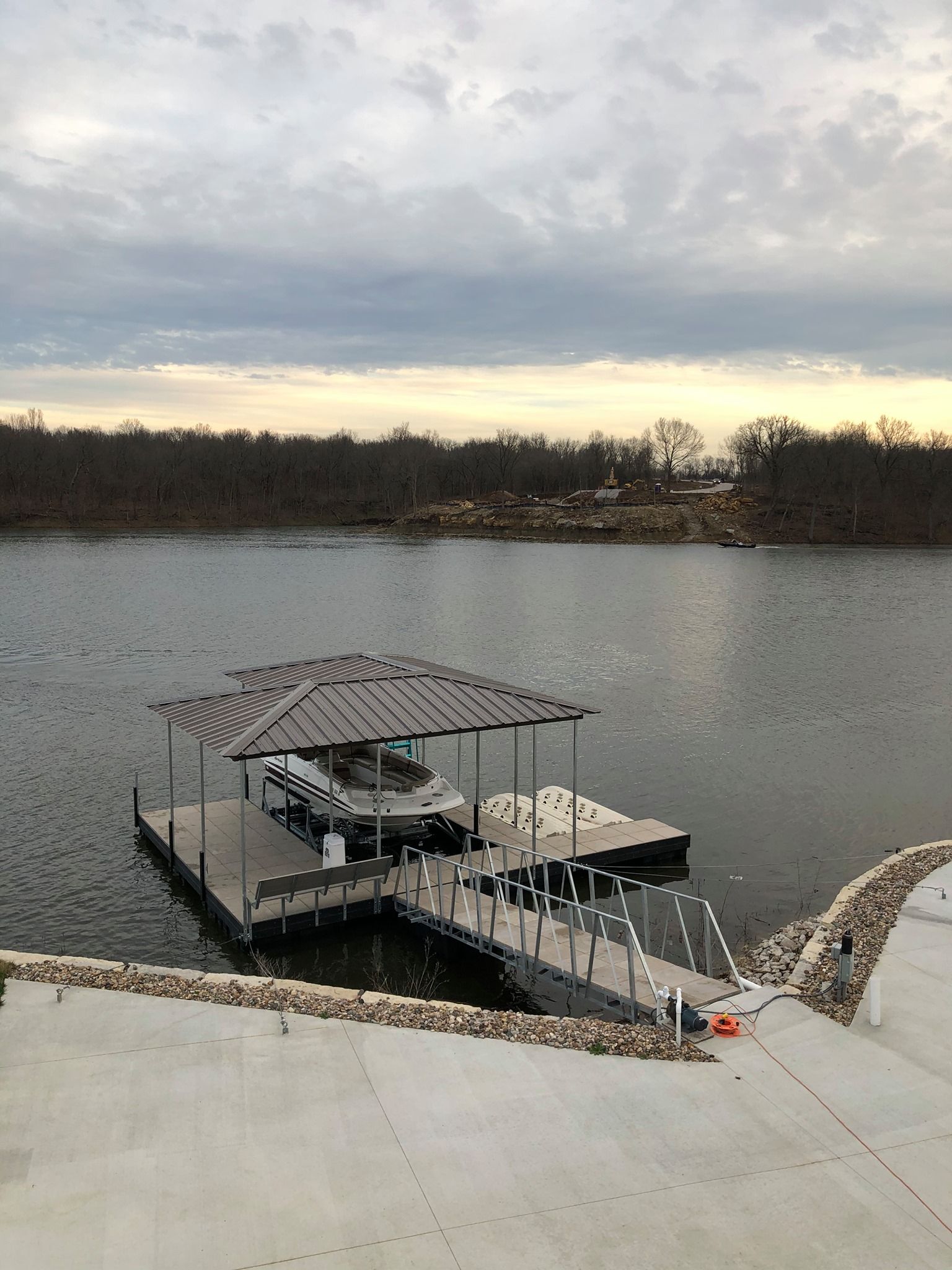 Covered dock on a lake at sunset, with calm water and cloudy sky.