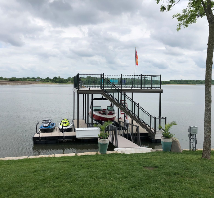 Small dock on a river with two jet skis, a boat, and stairs up to a platform with a flag.