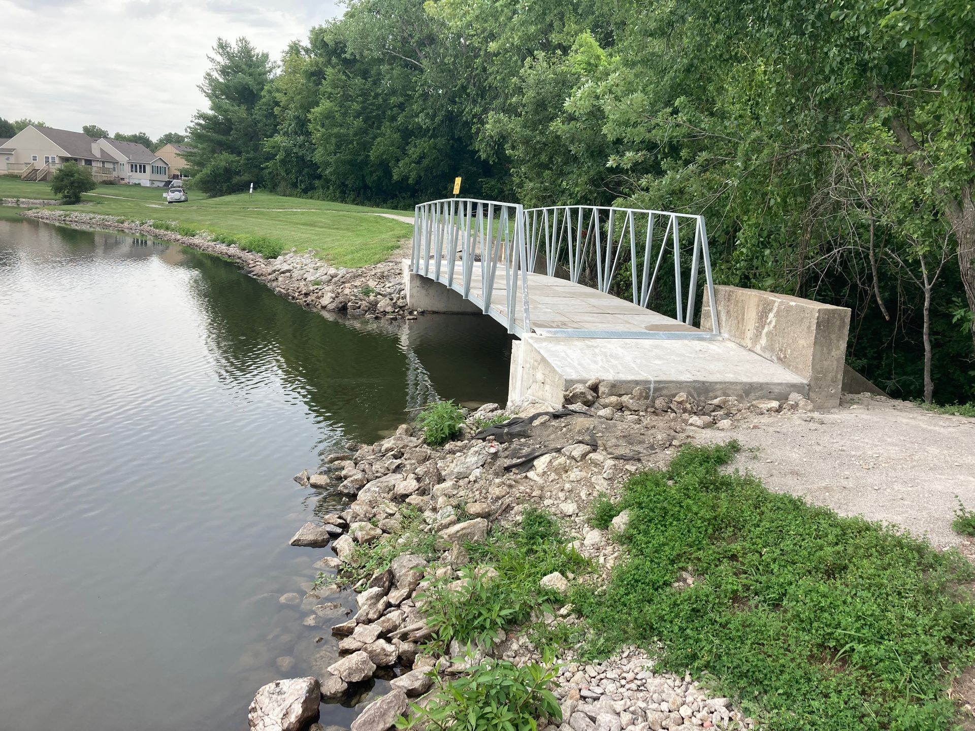 Small white footbridge over a calm river beside a rocky bank and green trees