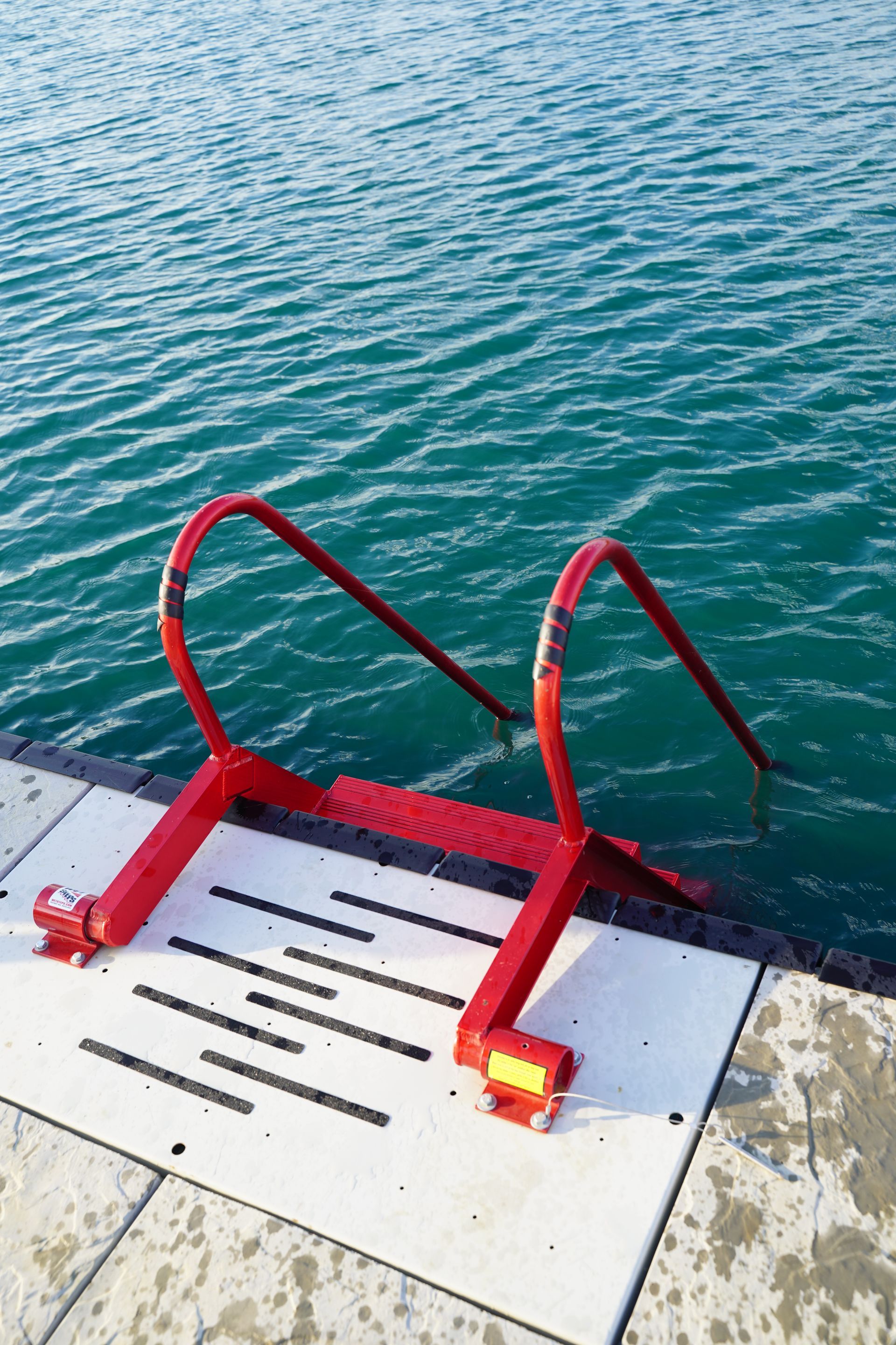 Red metal pool ladder with yellow light beside blue water at a dock edge