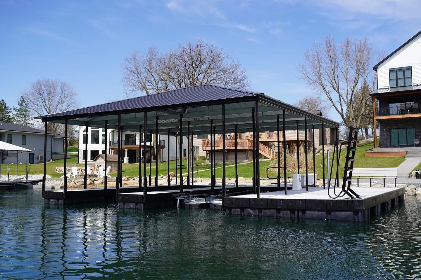 Modern lakeside pavilion with glass walls and black metal frame on a dock beside calm water