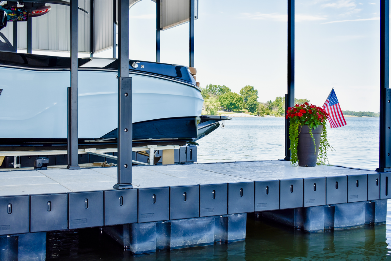 Boat docked beside a lakeside pier with potted flowers and a small American flag at sunset
