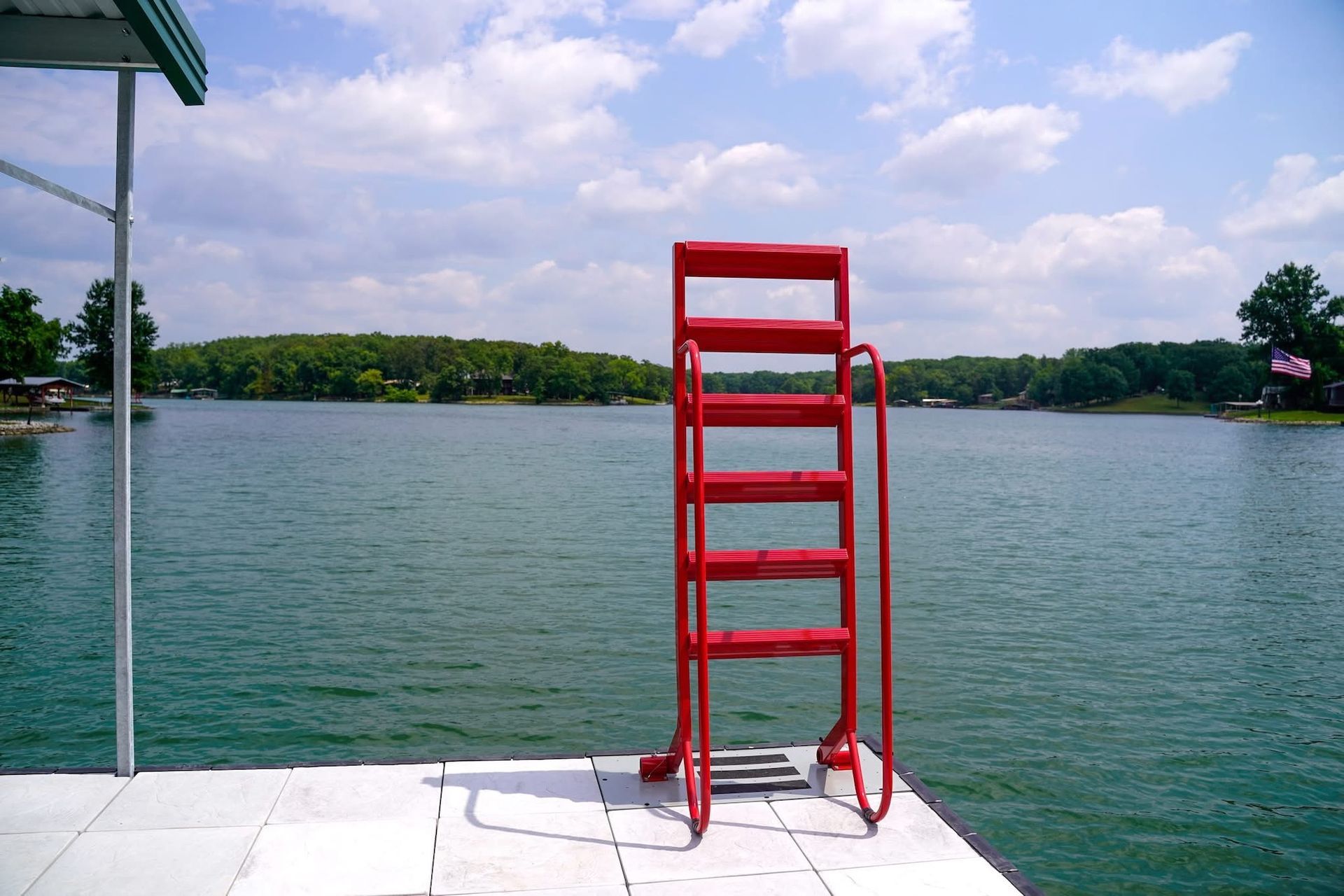 Red lifeguard chair on a dock overlooking a calm lake under a cloudy sky.