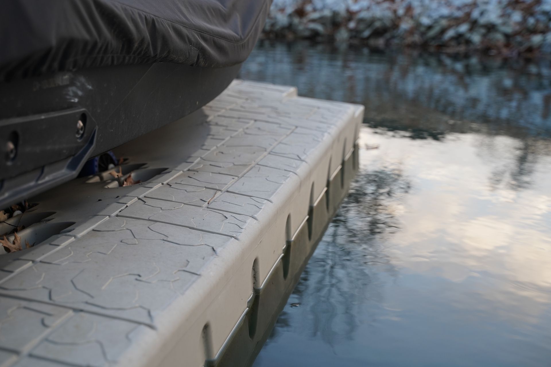 Cushioned dock edge beside calm water reflecting clouds, with a black boat seat at left.