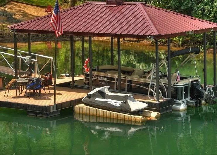 Lakeside dock with red-roof gazebo, chairs, a covered boat, and an American flag over green water