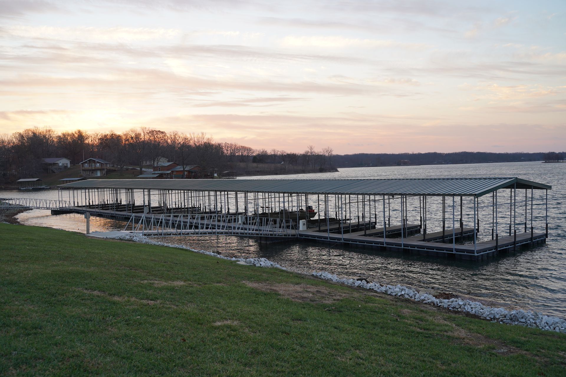 Wooden dock at a lakeshore at sunset, with calm water and a grassy foreground