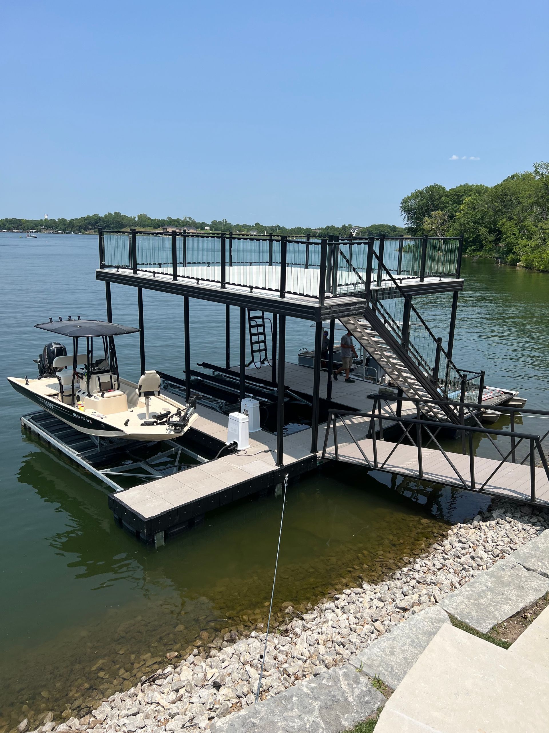 Floating dock and covered boat lift on a calm lakeshore with rocky shoreline and blue sky