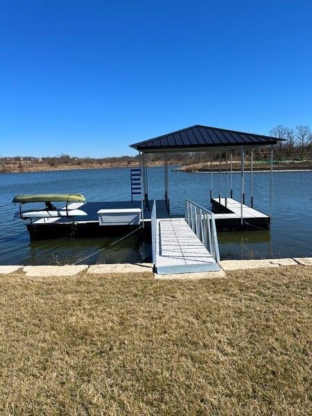 Lake dock with metal ramp and covered boat lift on calm water under a clear blue sky
